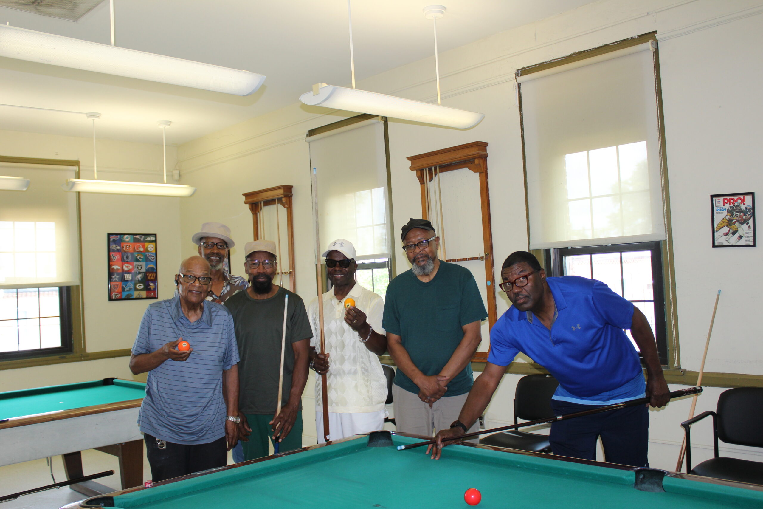 6 men gathering around a pool table.